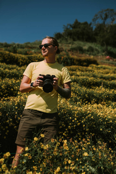 Man photographer in yellow tshirt standing in a field with yellow flowers in the north of Chiang Mai - Photo, image