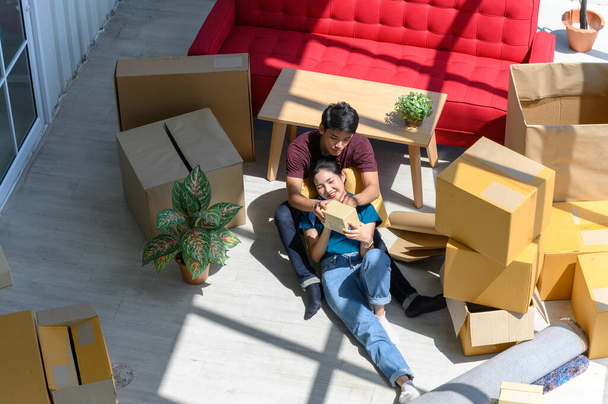 Vista superior de la joven pareja sonriendo, relajándose y descansando en el suelo después de desempacar cajas de cartón en una casa nueva con cajas de cartón en el suelo - Foto, imagen