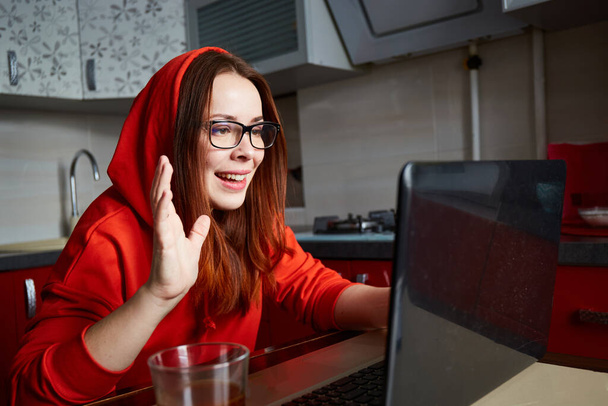 Conectados namoro. Retrato de mulher de cabelo vermelho satisfeito sentado na cozinha e fazendo chamada de vídeo no laptop - Foto, Imagem