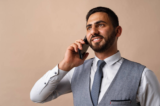 Arab businessman talking on his cellphone against beige background - Foto, afbeelding