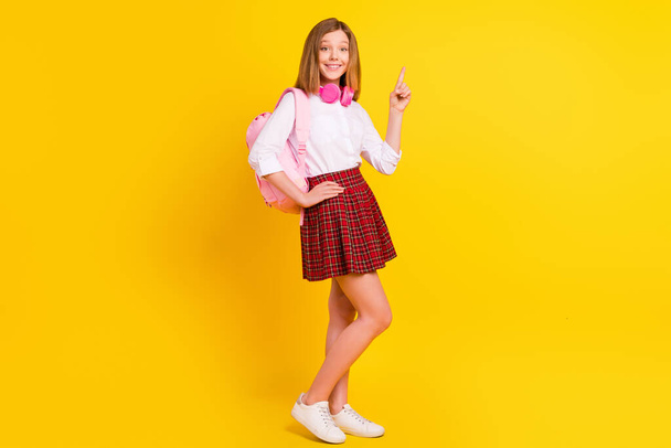 Full size photo of small girl point wear shirt skirt bag sneakers isolated on yellow color background - 写真・画像
