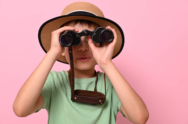 Lähikuva muotokuva poika kesällä olki hattu katselee läpi vanhoja vuosikerta kiikarit vastaan vaaleanpunainen tausta kopioi tilaa. Matkailu, matkailu, kesä, löytö ja seikkailu käsitteitä - Valokuva, kuva