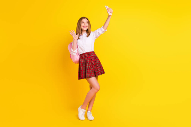 Full body photo of funny little girl do selfie wear shirt skirt bag sneakers isolated on yellow background - 写真・画像
