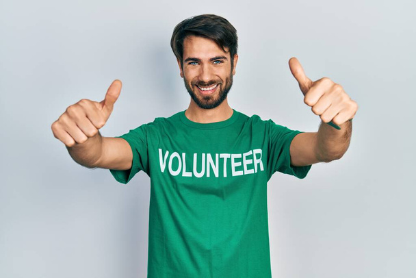 Junger hispanischer Mann im freiwilligen T-Shirt, der positive Gesten mit der Hand zustimmt, Daumen hoch lächelnd und glücklich über den Erfolg. Siegergeste.  - Foto, Bild