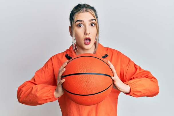 Молода сучасна дівчина тримає баскетбольний м'яч наляканий і шокований здивованим виразом, страхом і збудженим обличчям
.  - Фото, зображення