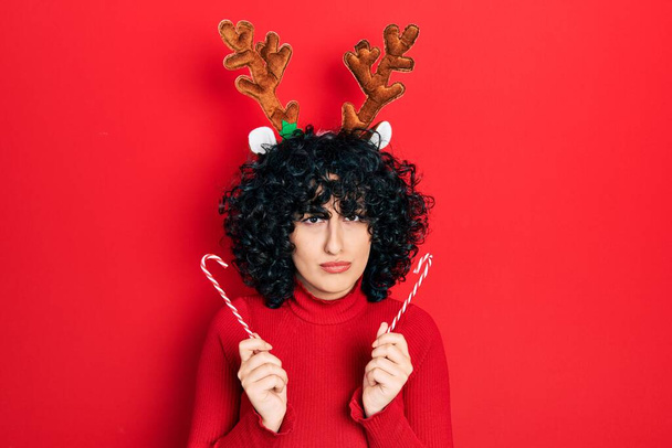 Jeune femme du Moyen-Orient portant de jolies cornes de rennes de Noël sceptiques et nerveuses, fronçant les sourcils bouleversés à cause d'un problème. personne négative.  - Photo, image