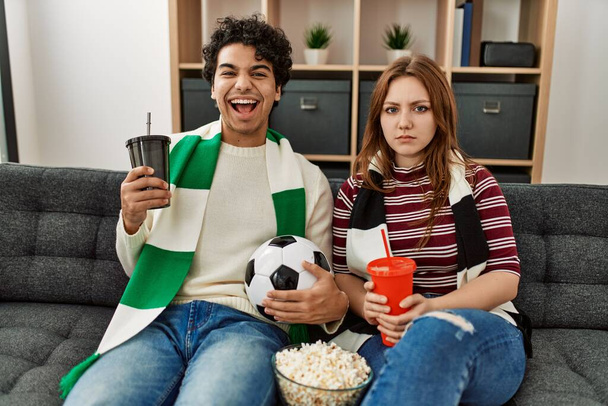 Молода пара хуліганів, що підтримують футбольну команду, сидить на дивані вдома
. - Фото, зображення