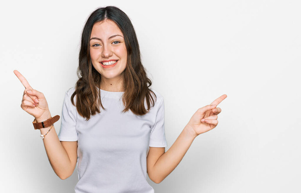 Молодая красивая женщина в обычной белой футболке улыбается уверенно указывая пальцами в разные стороны. копировальное место для рекламы  - Фото, изображение