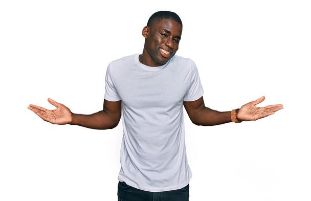 Young african american man wearing casual white t shirt smiling showing both hands open palms, presenting and advertising comparison and balance  - 写真・画像