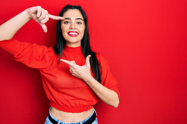 Young hispanic girl wearing casual clothes smiling making frame with hands and fingers with happy face. creativity and photography concept.  - Photo, Image
