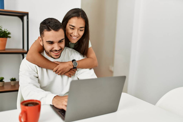 Joven pareja latina usando laptop y tomando café en casa. - Foto, Imagen