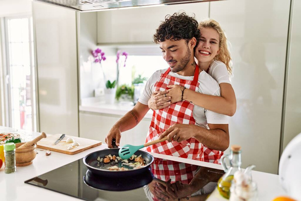 Young couple smiling happy and hugging cooking at kitchen. - Foto, immagini