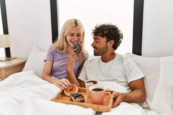 Young beautiful couple smiling happy having breakfast on the bed at home. - Foto, Imagem