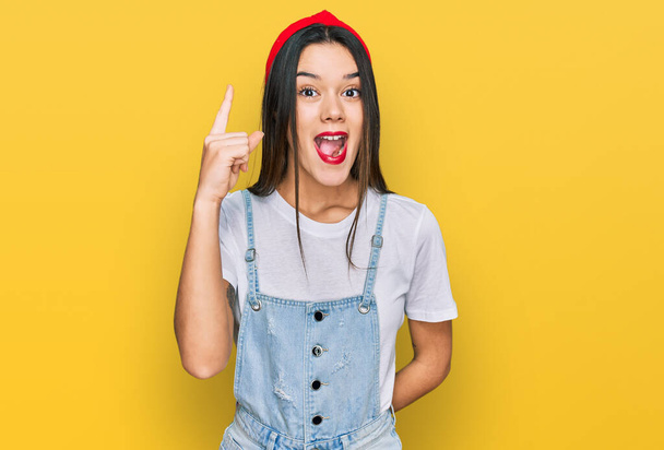 Jong Latijns-Amerikaans meisje draagt casual kleding wijzend met de vinger omhoog met een succesvol idee. opgewonden en gelukkig. Nummer een.  - Foto, afbeelding