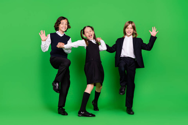 Full body photo of impressed small girl boys hold hands go wave wear school uniform isolated on green background - 写真・画像