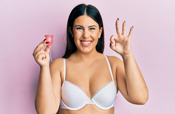 Beautiful brunette woman holding menstrual cup wearing underwear sticking tongue out happy with funny expression.  - Photo, Image