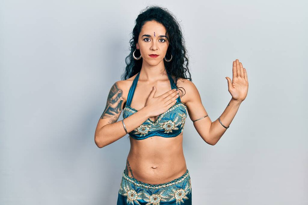 Junge Frau in Bindi und traditioneller Bauchtanzkleidung schwört mit der Hand auf Brust und Handfläche und leistet Treueschwur  - Foto, Bild