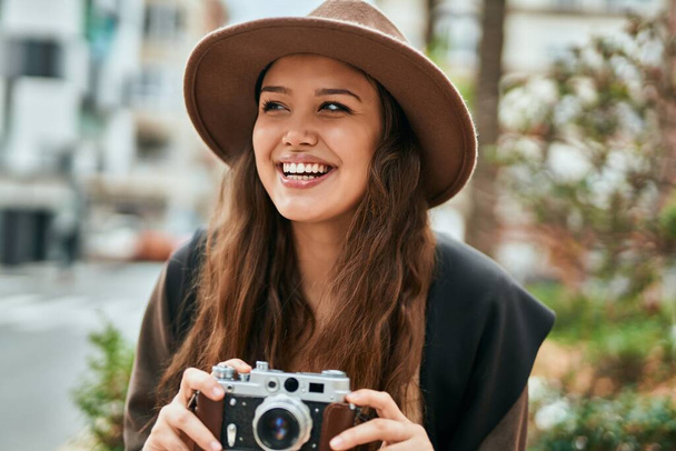 Молодая испаноязычная туристка улыбается счастливой, используя винтажную камеру в городе. - Фото, изображение