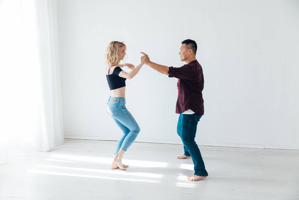 Ένας άντρας και μια γυναίκα χορεύουν μπάτσατα με μουσική σε ένα λευκό δωμάτιο. - Φωτογραφία, εικόνα