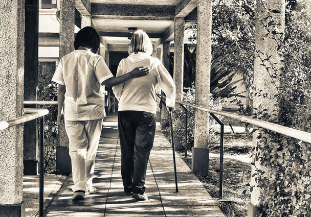 Asiatischer Arzt hilft einer älteren Rentnerin mit Rollator auf dem Hof des Krankenhauses. Sanierungskonzept. - Foto, Bild
