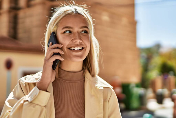 Junges blondes Mädchen lächelt fröhlich auf dem Smartphone in der Stadt. - Foto, Bild