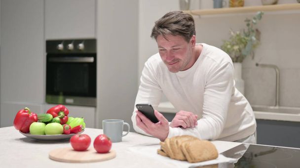 Middle Aged Man using Smartphone while in Kitchen - Photo, image