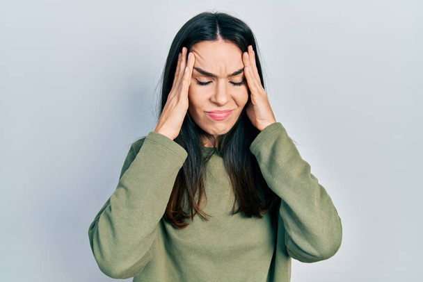 Young brunette woman wearing casual green sweater suffering from headache desperate and stressed because pain and migraine. hands on head.  - Фото, зображення