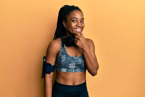 African american woman with braided hair wearing sportswear and arm band looking confident at the camera smiling with crossed arms and hand raised on chin. thinking positive.  - Foto, afbeelding