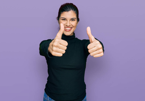 Молодая латиноамериканка в повседневной одежде, одобряющая позитивный жест рукой, улыбается и радуется успеху. жест победителя.  - Фото, изображение