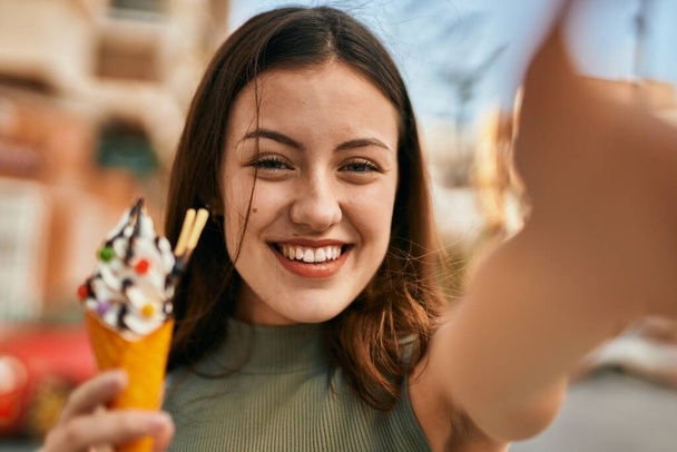 Young caucasian girl eating ice cream making selfie by the camera at the city. - 写真・画像