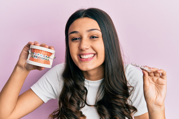 Young hispanic woman holding invisible aligner orthodontic and braces smiling and laughing hard out loud because funny crazy joke.  - Photo, Image