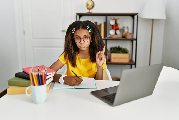 Junge afrikanisch-amerikanische Mädchen bei den Hausaufgaben zu Hause zeigt nach oben Blick traurig und verärgert, zeigt die Richtung mit den Fingern, unglücklich und deprimiert.  - Foto, Bild