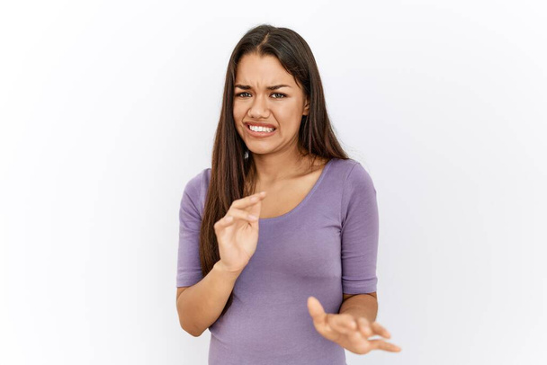 Young brunette woman standing by isolated background disgusted expression, displeased and fearful doing disgust face because aversion reaction. with hands raised  - Foto, Imagen