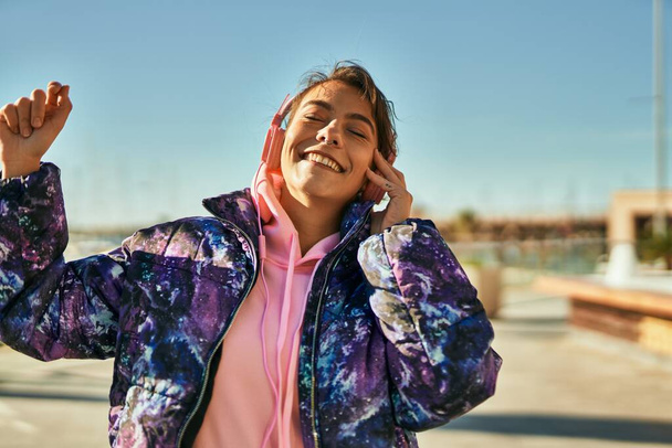 街でヘッドフォンダンスを使用して幸せな笑顔若いヒスパニック系スポーティな女性. - 写真・画像