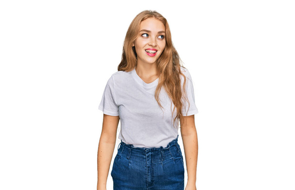 Fiatal kaukázusi lány alkalmi fehér pólóban, aki oldalra néz mosollyal az arcán, természetes kifejezéssel. nevetés magabiztos.  - Fotó, kép