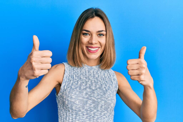 Young caucasian blonde woman wearing casual t shirt success sign doing positive gesture with hand, thumbs up smiling and happy. cheerful expression and winner gesture.  - Photo, Image