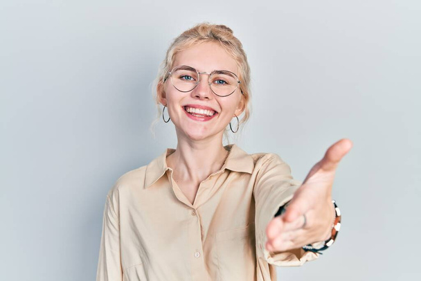 Beautiful caucasian woman with blond hair wearing casual look and glasses smiling friendly offering handshake as greeting and welcoming. successful business.  - Photo, Image