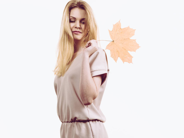 Fashionable autumn long hair blonde girl holding autumnal dry brown maple leaf in hand. Autumn, season and forecasting concept. - Fotó, kép