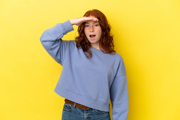 Teenager načervenalé žena izolované na žlutém pozadí dělá překvapení gesto při pohledu dopředu - Fotografie, Obrázek