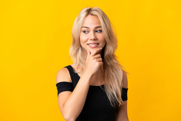 Νεαρή Ρωσίδα απομονωμένη σε κίτρινο φόντο κοιτώντας στο πλάι και χαμογελώντας - Φωτογραφία, εικόνα