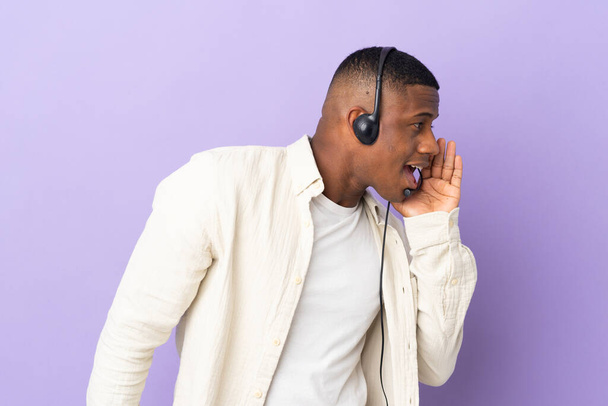 Telemarketer latin man working with a headset isolated on purple background shouting with mouth wide open to the side - Foto, immagini