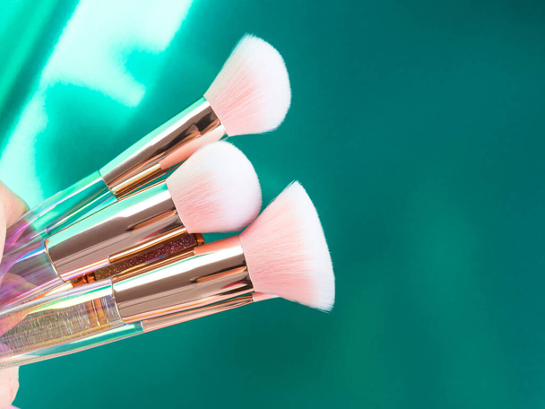 Trendy make up shiny pink brushes on green metallic background - Photo, image