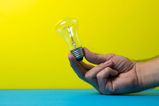 Hand holds an incandescent lamp on a colored background. Idea and development concept - Photo, Image