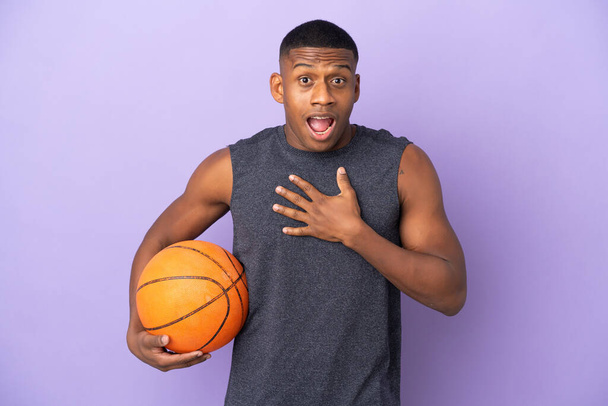 Junge Basketballspieler Mann isoliert auf lila Hintergrund überrascht und schockiert, während Sie rechts - Foto, Bild