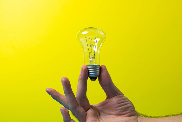 La mano sostiene una lámpara incandescente sobre un fondo de color. Concepto de ideas y desarrollo - Foto, Imagen