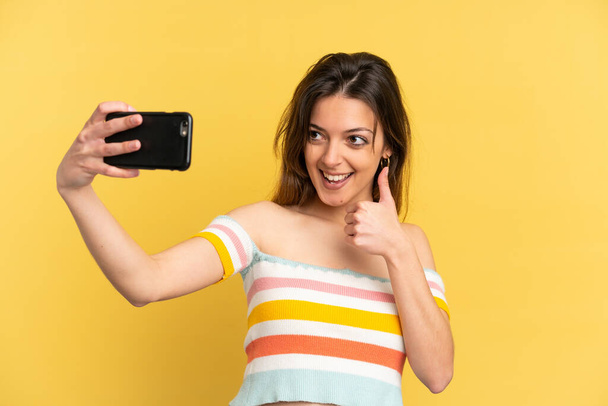 Young caucasian woman isolated on yellow background making a selfie with mobile phone - Foto, afbeelding