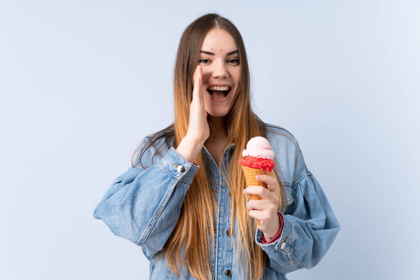 Νεαρή γυναίκα με ένα παγωτό κορνέτα απομονωμένη σε μπλε φόντο φωνάζοντας με ανοιχτό το στόμα - Φωτογραφία, εικόνα