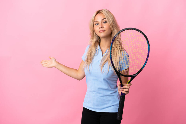 Giovane donna russa che gioca a tennis isolato su sfondo viola allungando le mani di lato per invitare a venire - Foto, immagini
