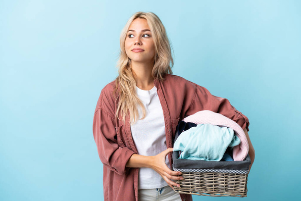 Young Russian woman holding a clothes basket isolated on blue background . Portrait - Fotoğraf, Görsel