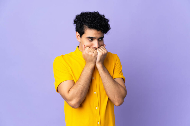 Young Venezuelan man isolated on purple background nervous and scared putting hands to mouth - Foto, afbeelding